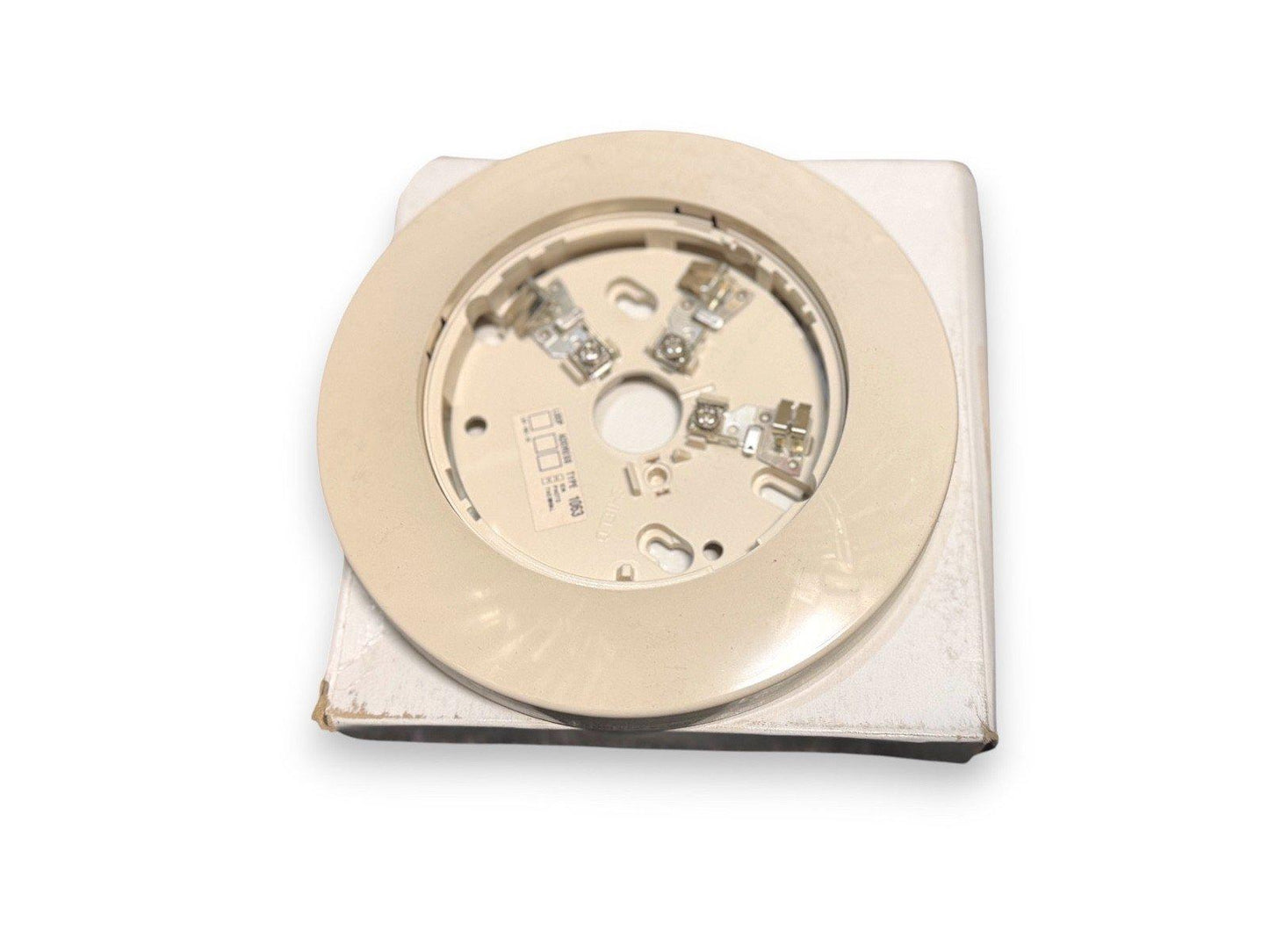 Beige fire alarm base with terminal connectors, shown on packaging for fire safety equipment