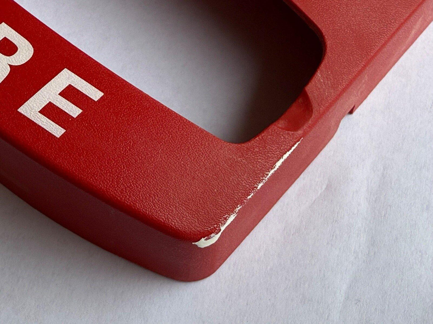 Red fire alarm pull station cover with white lettering, showing slight wear on edge