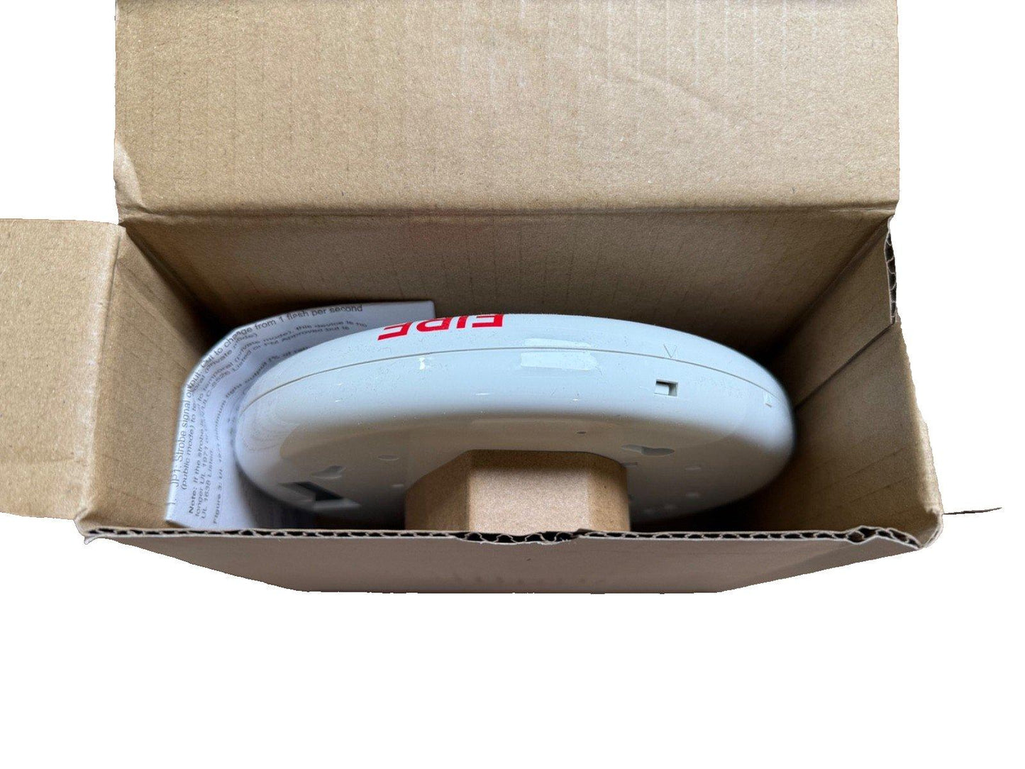 White fire alarm strobe light in open box, labeled 'FIRE', for commercial or residential safety systems.