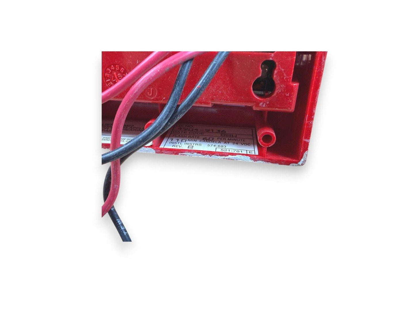Red fire alarm device with wiring, specs label showing 24 VDC, 110 min candela output
