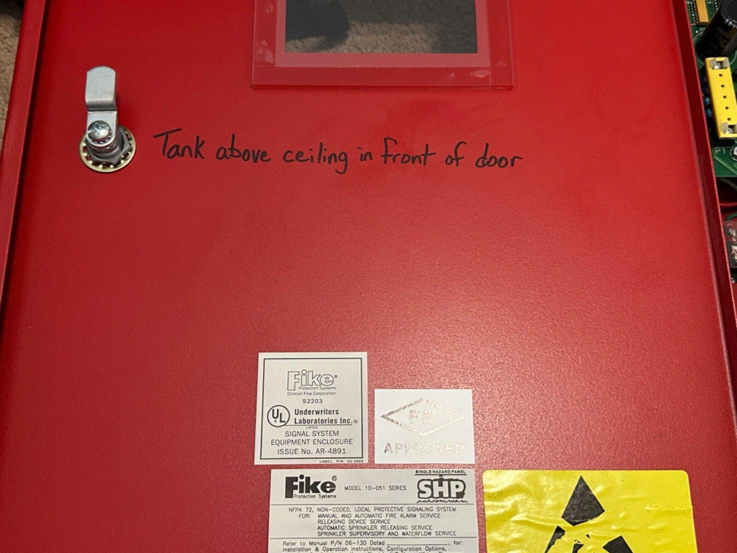 Red Fike fire alarm control panel with UL and FM approval labels, handwritten tank location note