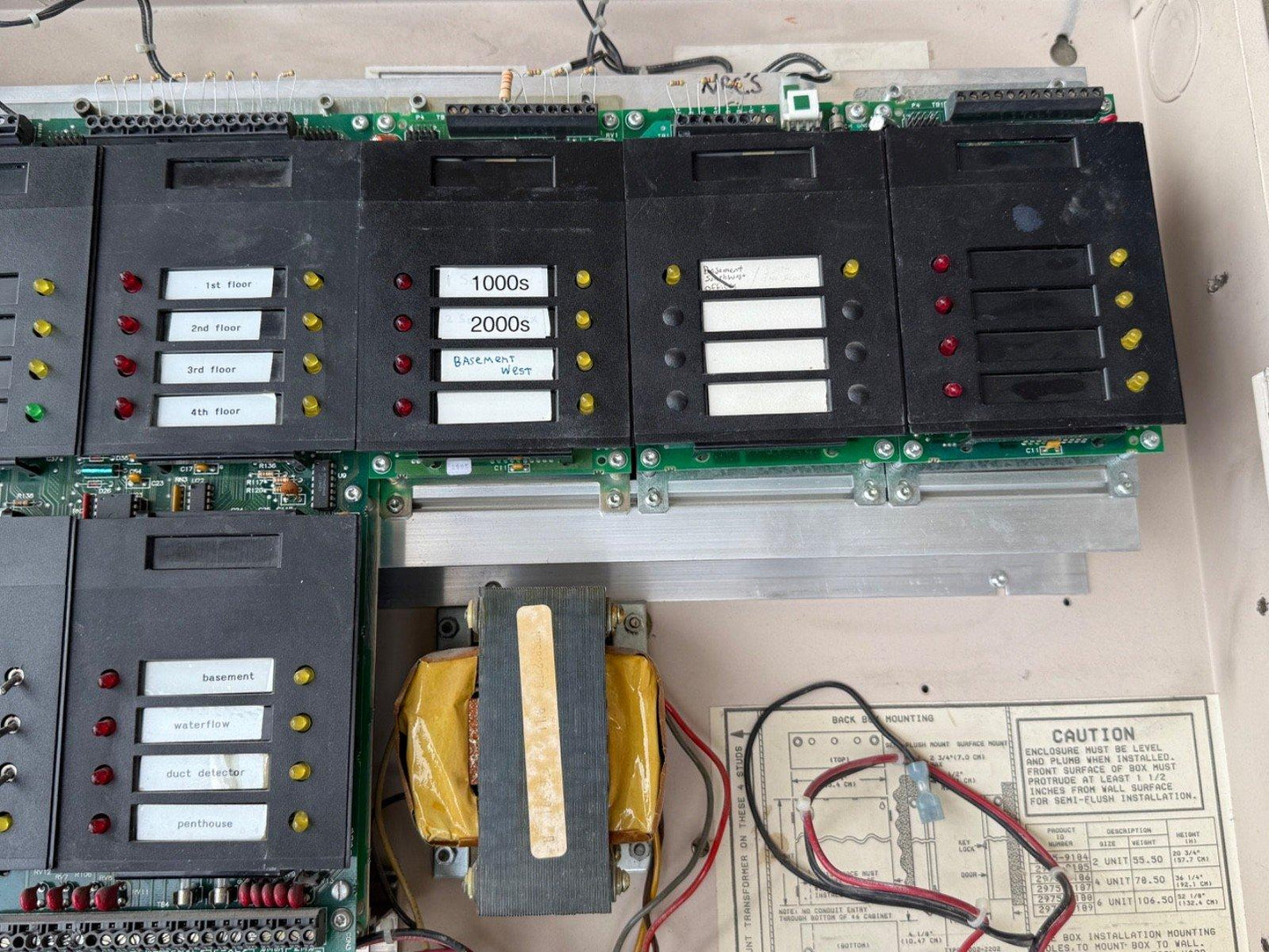 Fire alarm control panel with labeled zones, indicator lights, and transformer, for commercial building safety systems.