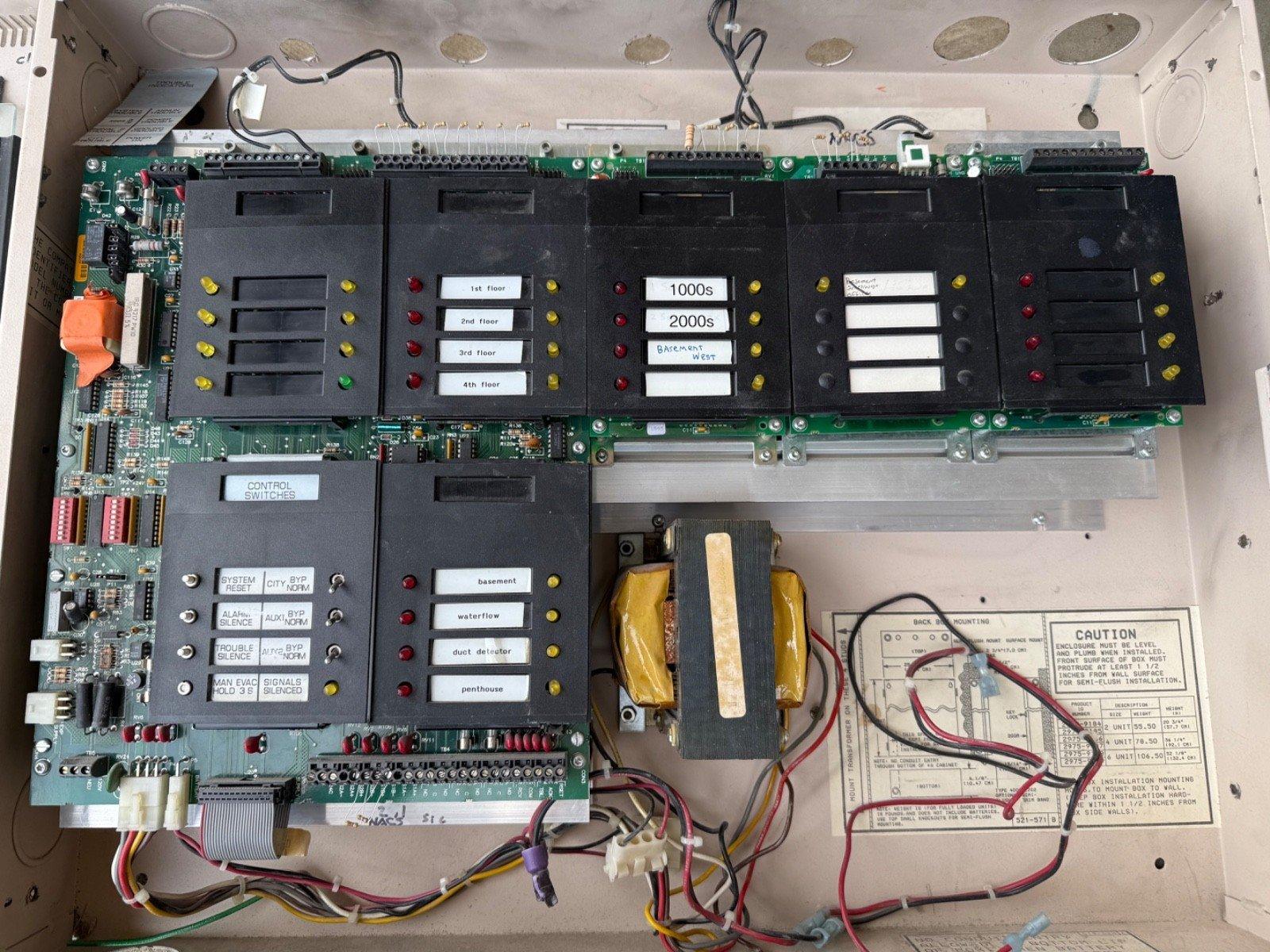 Fire alarm control panel with circuit boards, labeled zones, switches, and wiring for commercial building safety systems