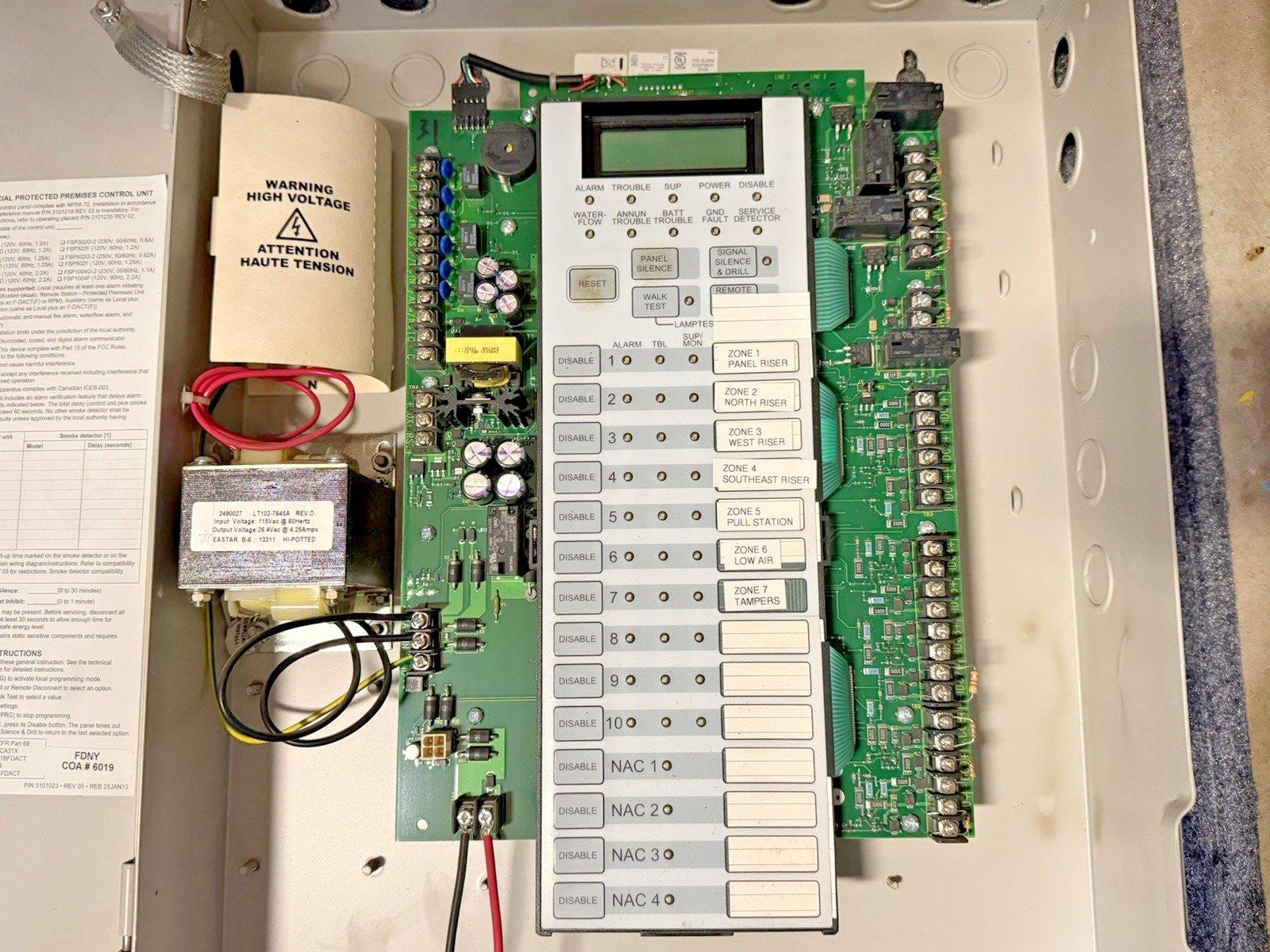 Fire alarm control panel with circuit board, zone indicators, and high voltage warning label