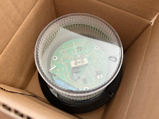 Fire alarm strobe light with visible circuit board inside cardboard box, new surplus equipment