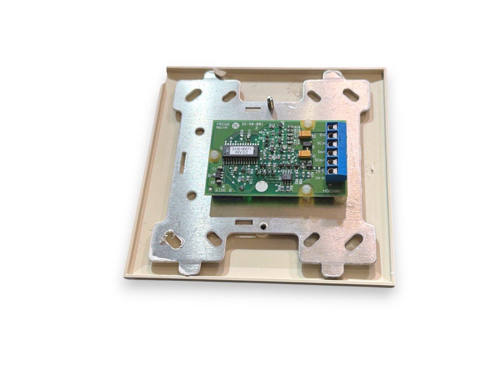 Fire alarm control module with green circuit board and blue terminal block, mounted in metal bracket