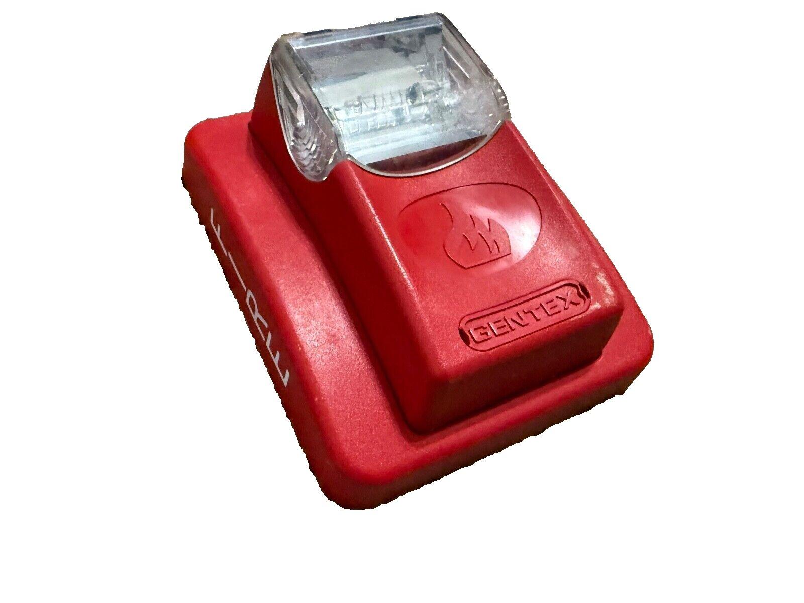 Red Gentex fire alarm strobe light with clear lens and flame icon, for commercial safety systems