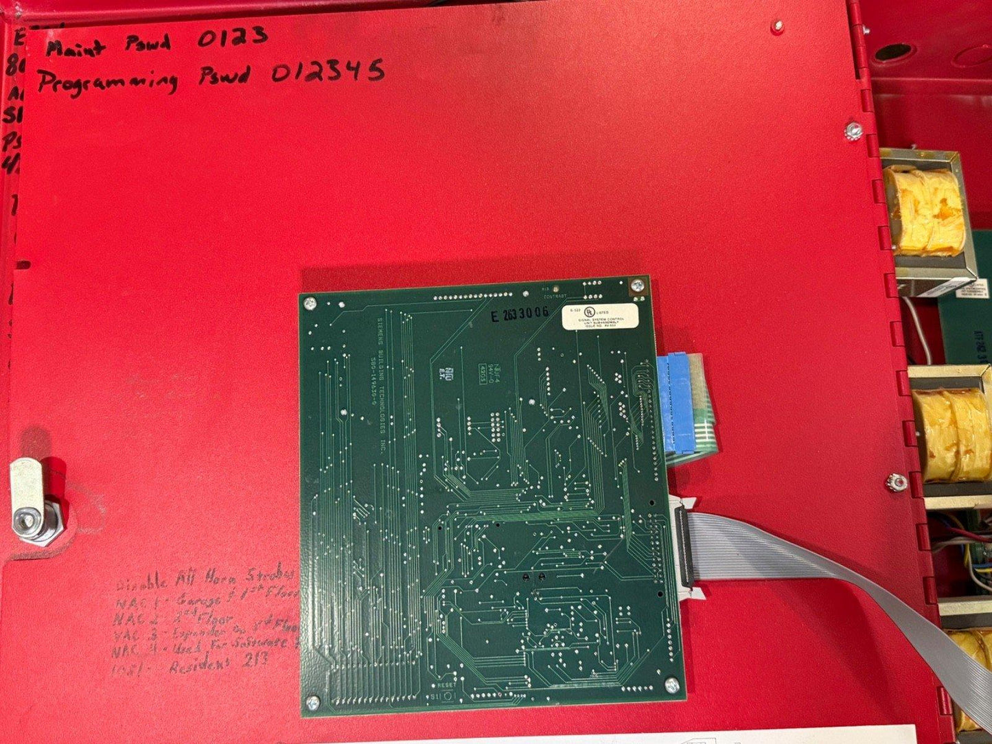 Fire alarm control panel circuit board with handwritten passwords and wiring inside red enclosure