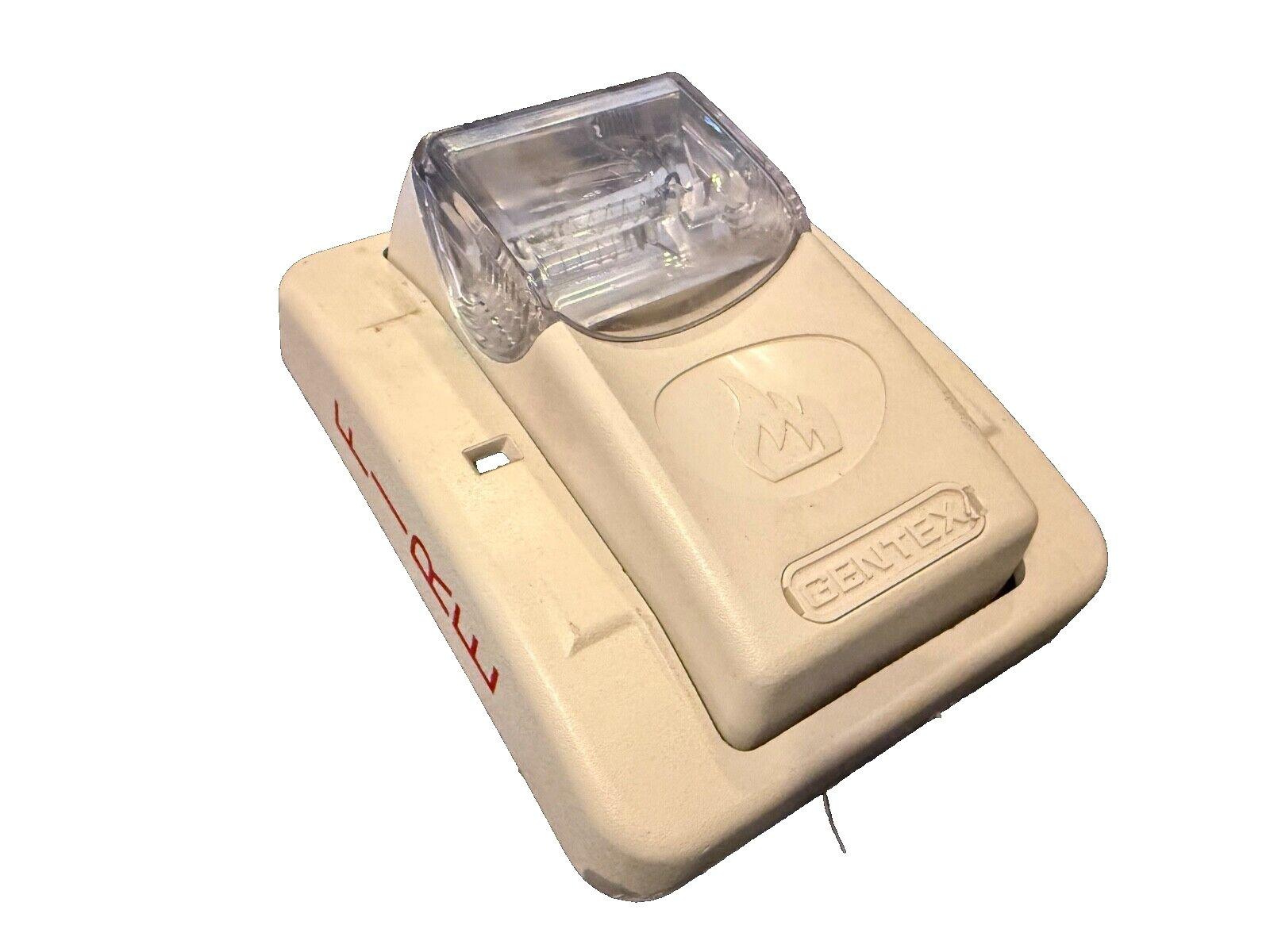 Gentex fire alarm strobe light with clear lens and flame symbol, beige housing for emergency signaling