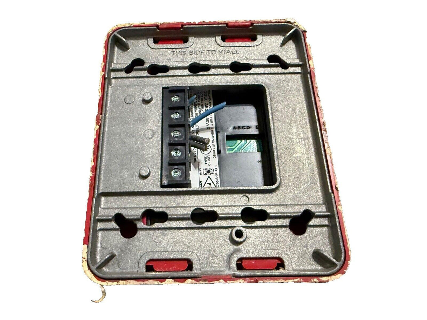 Fire alarm device back panel with wiring terminals and mounting holes, labeled 'THIS SIDE TO WALL'
