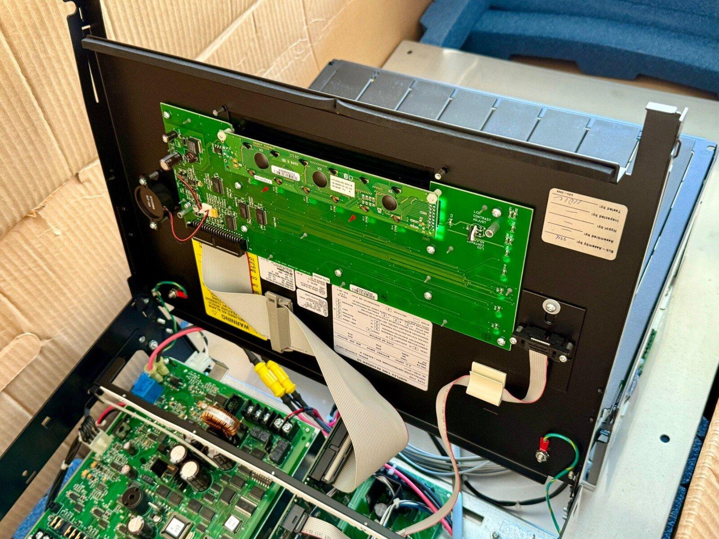 Open fire alarm control panel with green circuit boards and wiring, showing internal components for installation or repair.