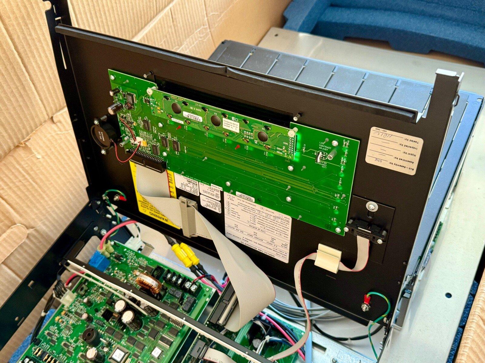 Open fire alarm control panel with green circuit boards and wiring, showing internal components for installation or repair.