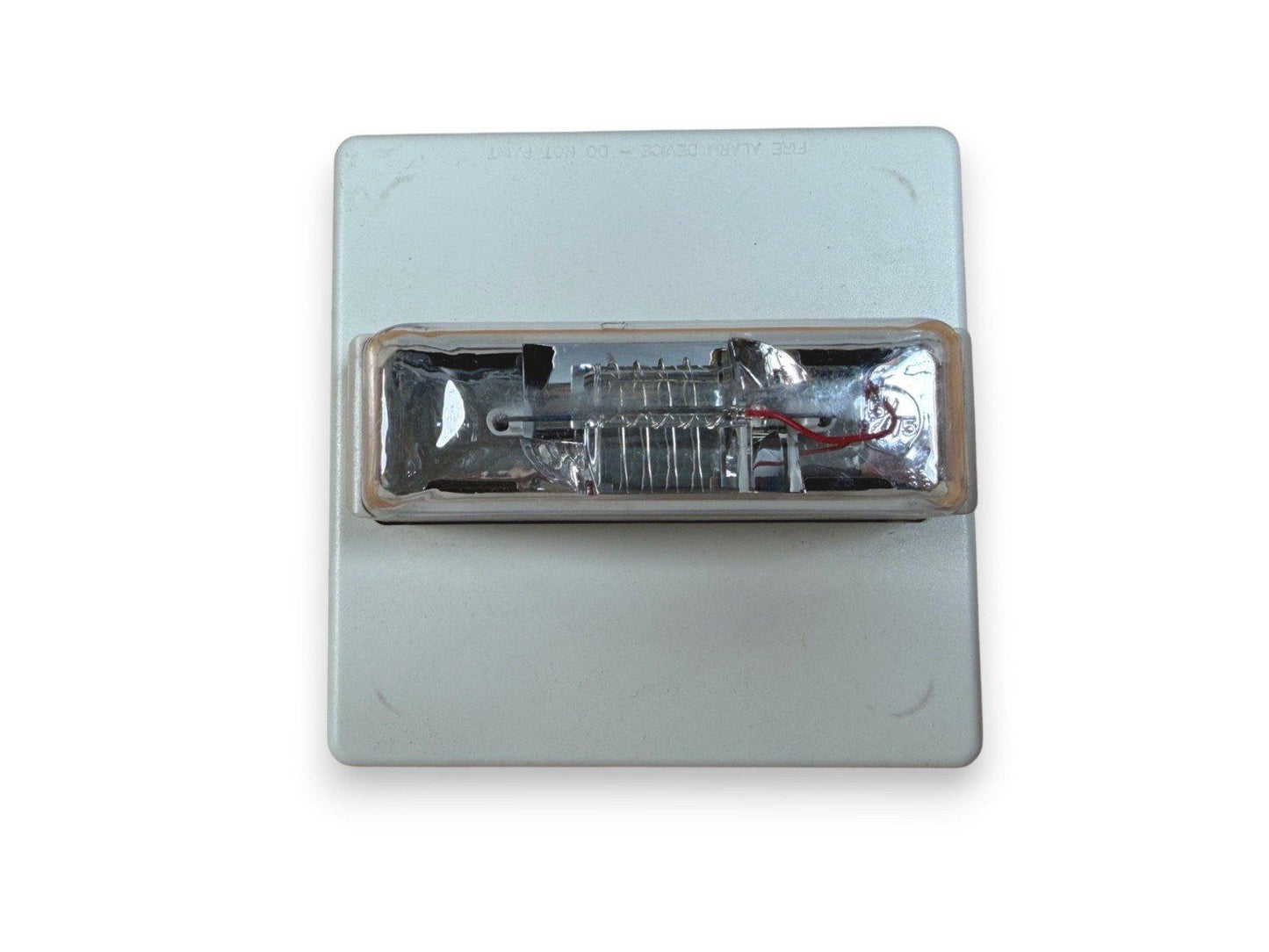 Fire alarm strobe light with clear lens and internal wiring, mounted on white base