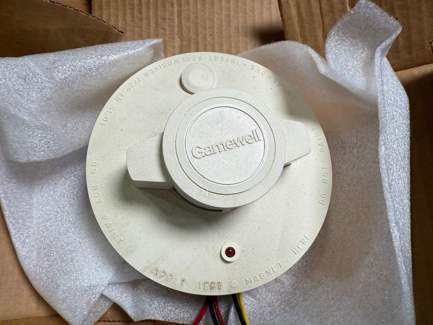 Gamewell fire alarm device with test magnet slot, red LED, and wiring, nestled in bubble wrap inside box