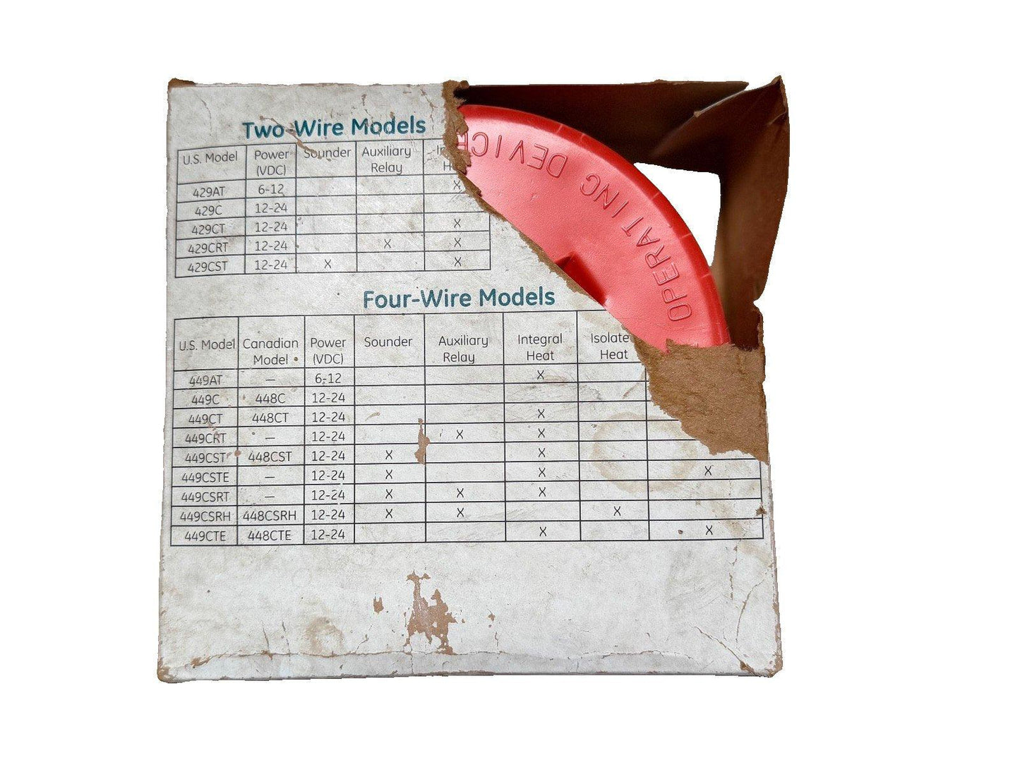 Red fire alarm device in open box with two-wire and four-wire model specs visible