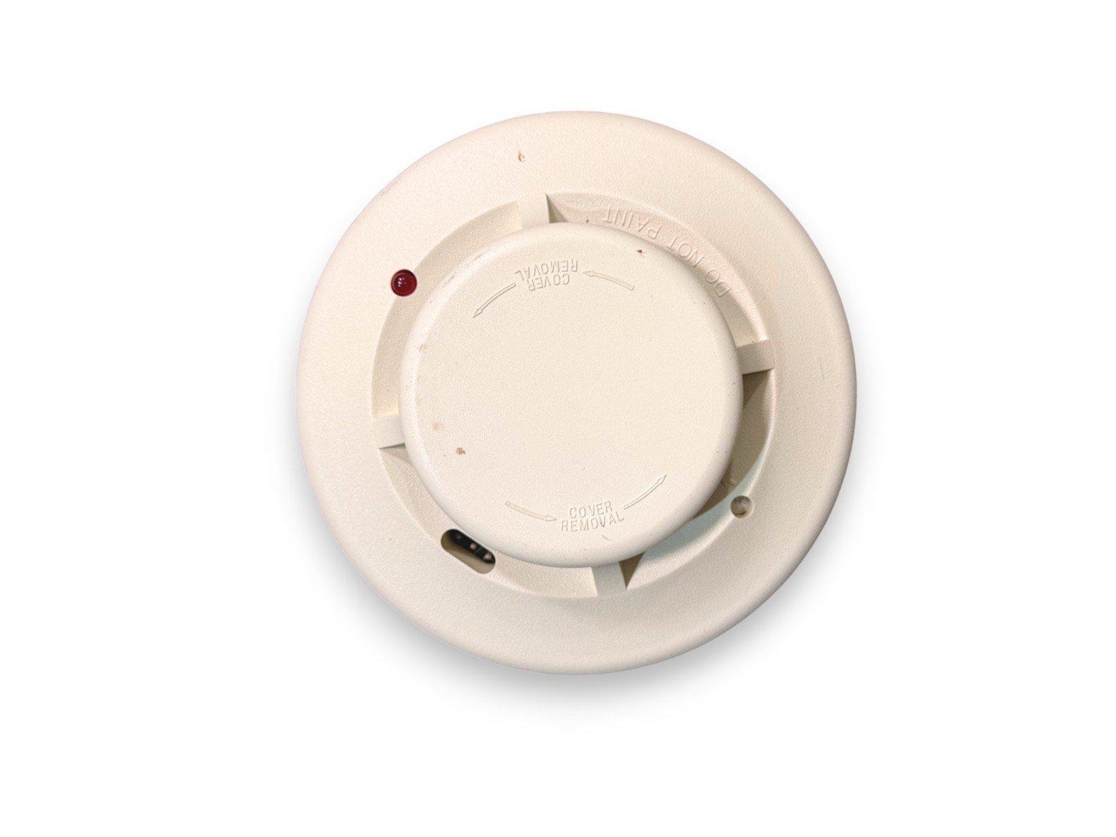 White smoke detector with red LED indicator and cover removal slots for fire alarm systems