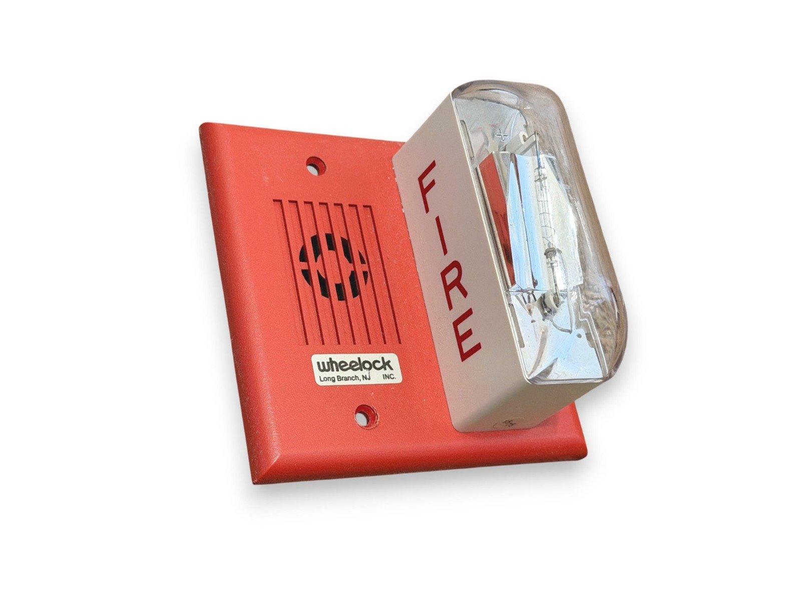 Wheelock fire alarm horn strobe with red housing and clear lens, labeled FIRE for emergency alerts