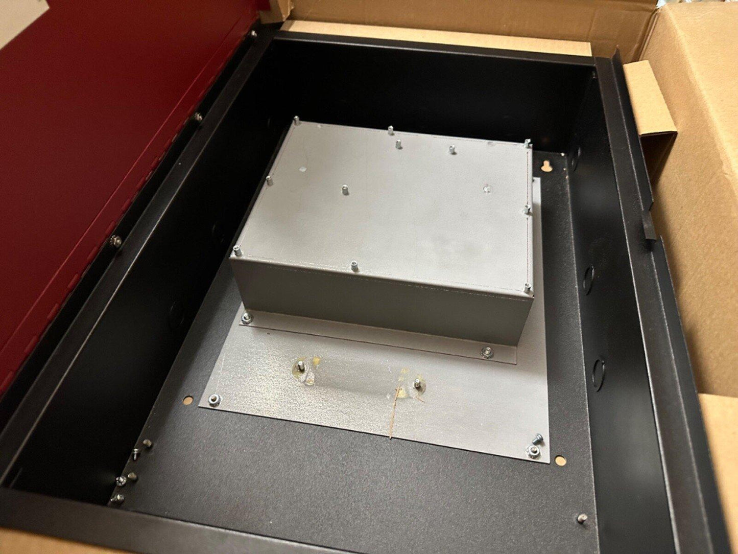 Fire alarm control panel enclosure with mounted metal box, inside open cardboard packaging