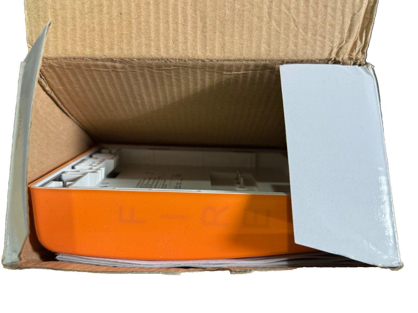 Orange fire alarm control panel in open cardboard box, ready for installation or repair