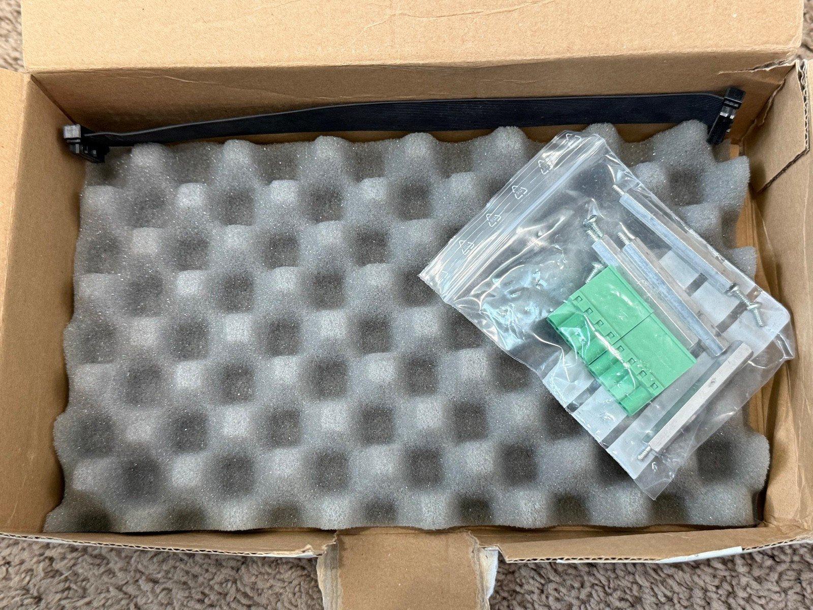 Fire alarm mounting kit with green terminal block, screws, and black strap in foam-packed box