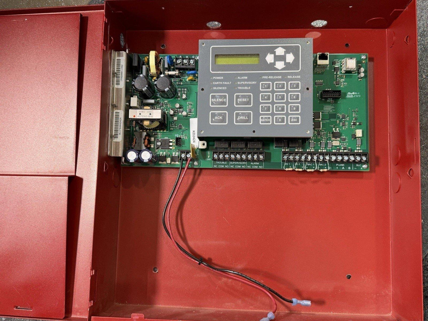 Fire alarm control panel with keypad, circuit board, and wiring inside red enclosure