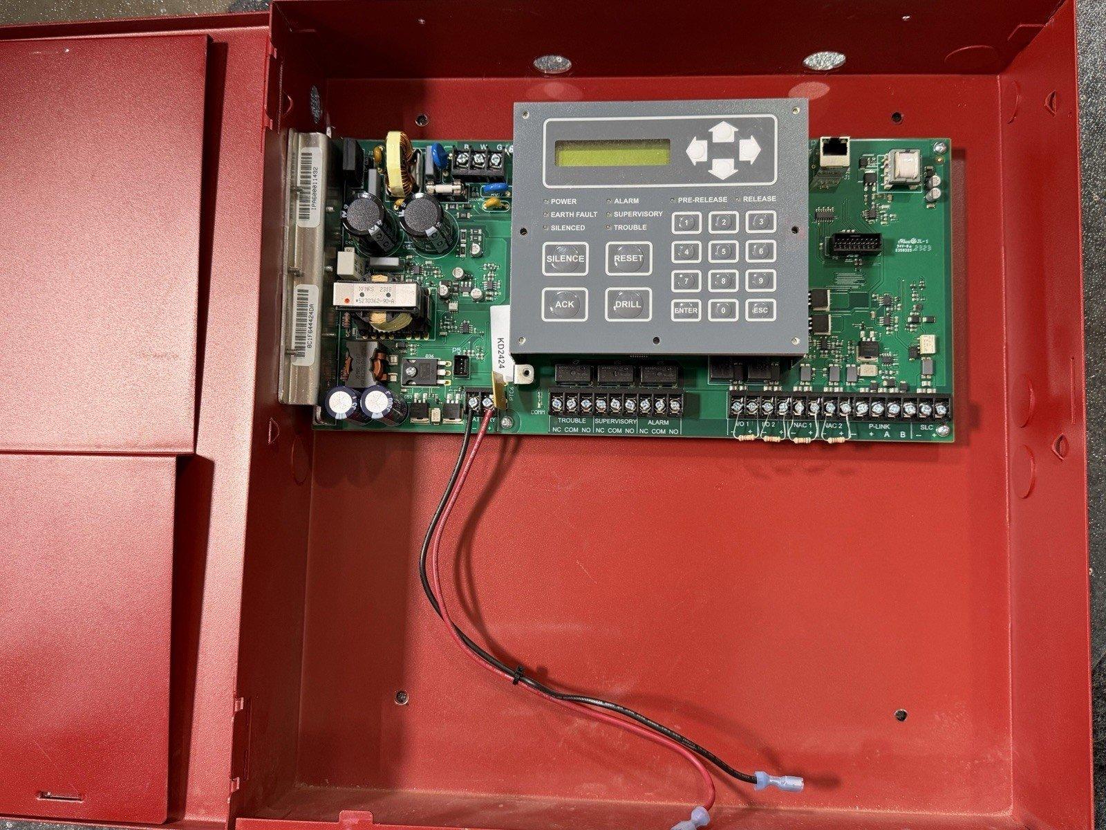 Fire alarm control panel with keypad, circuit board, and wiring inside red enclosure