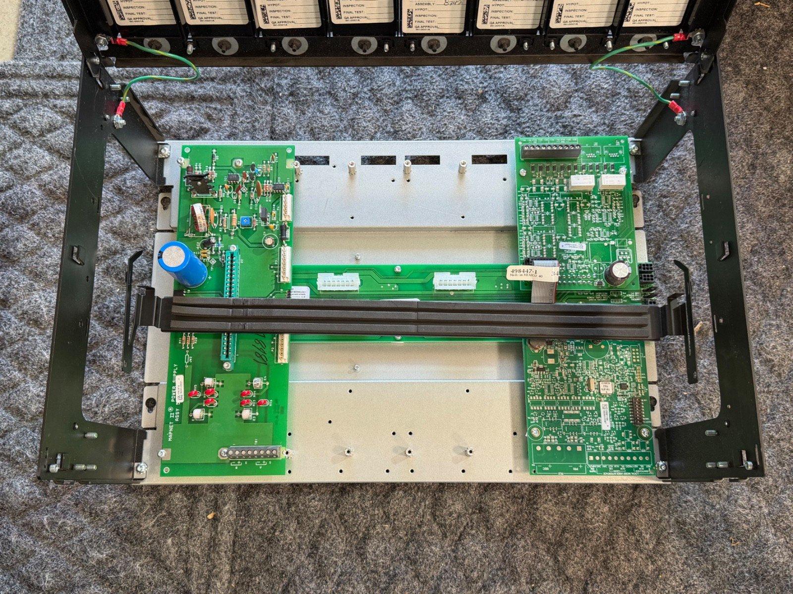 Fire alarm control panel with green circuit boards and wiring, showing internal components for fire safety systems.